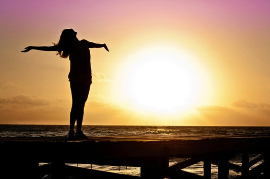 femme qui leve les bras au ciel au coucher du soleil