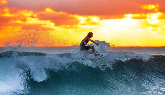 une personne fait du surf sur une vague durant le couché du soleil