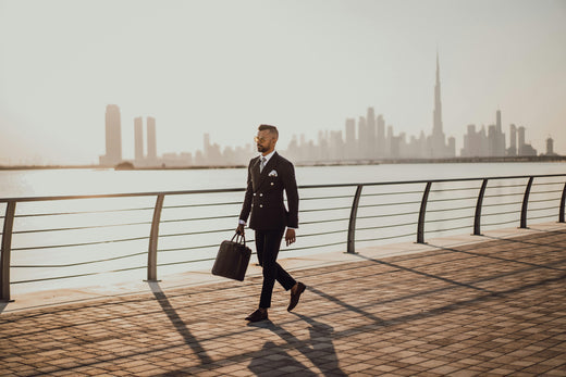 un homme en costume sac á la main marche devant la skyline de Dubai