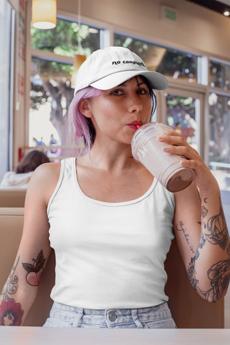 femme stylée assise entrain de boire un verre elle porte une casquette blanche Ayoun ecrit"No comment"